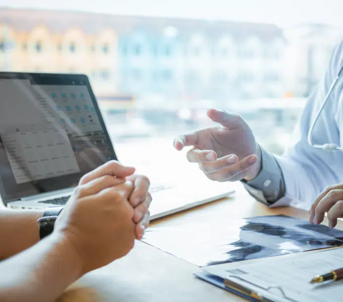 Healthcare professional consulting with a patient at a desk with a laptop